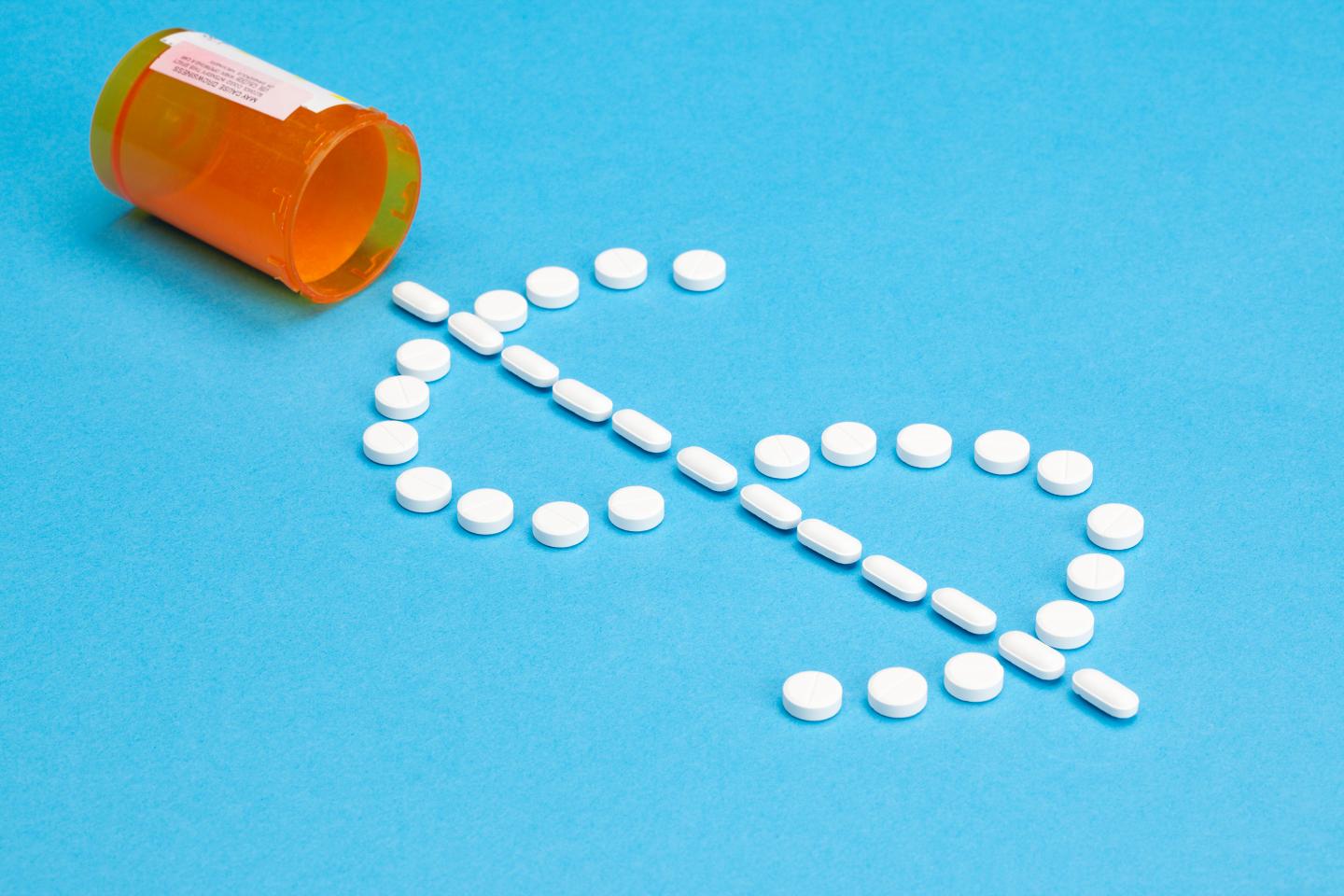 White pills in the shape of a dollar sign spilling from a prescription pill bottle onto a blue background.