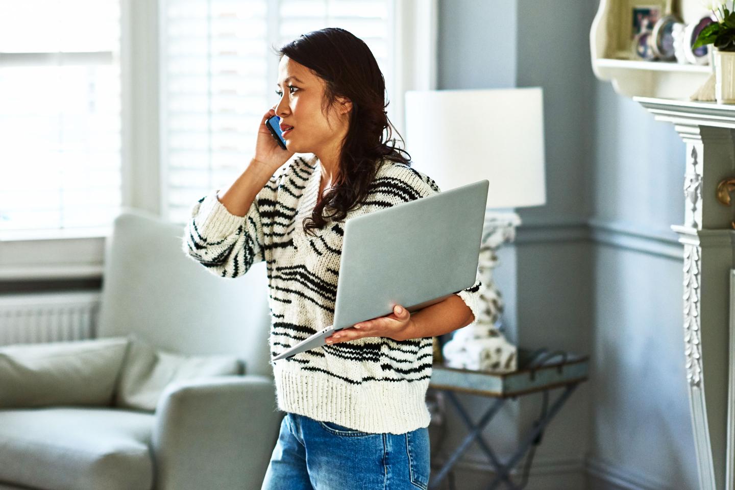 Woman holding laptop and listening on smartphone