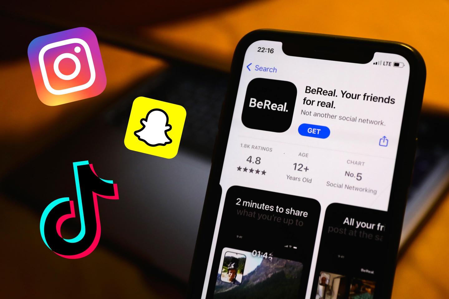 BeReal on the App Store displayed on a phone screen and a laptop in the background with icons for Instagram, Snapchat and TikTok