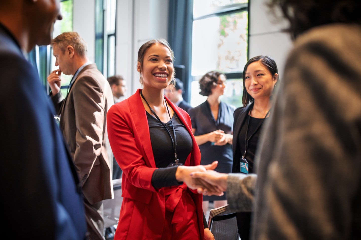 Woman in a red suit shakes hands with another business women while at a conference