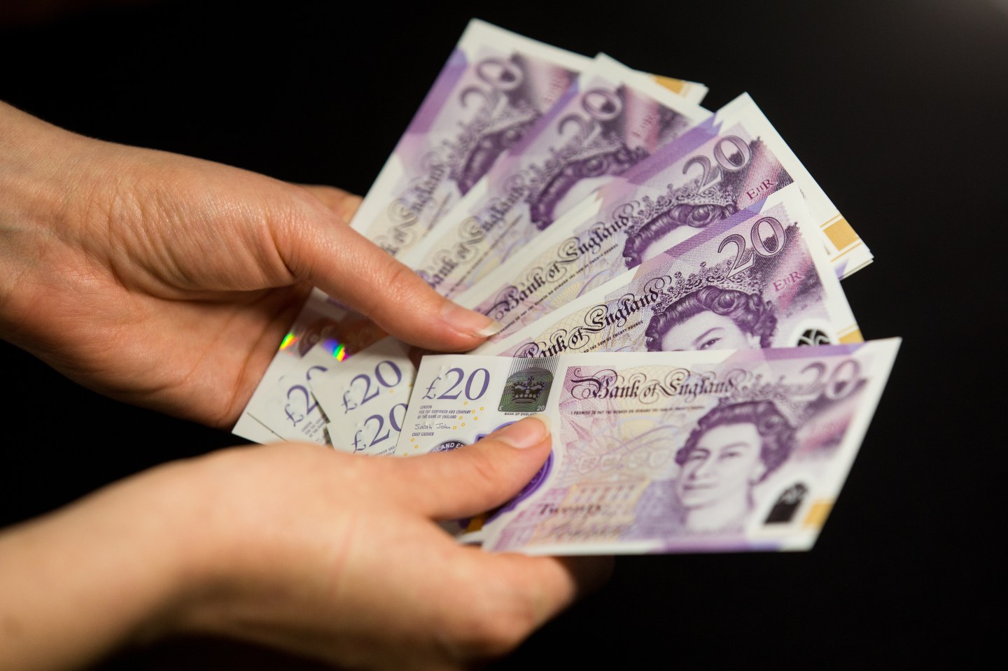 An unseen person holds multiple £20 notes.