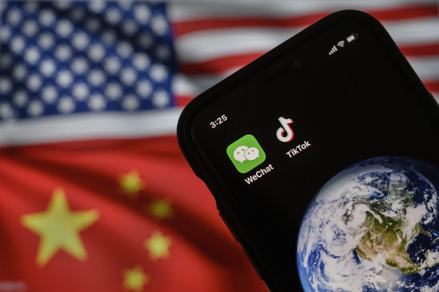 a mobile phone can be seen displaying the logos for Chinese apps WeChat and TikTok in front of a monitor showing the flags of the United States and China on an internet page