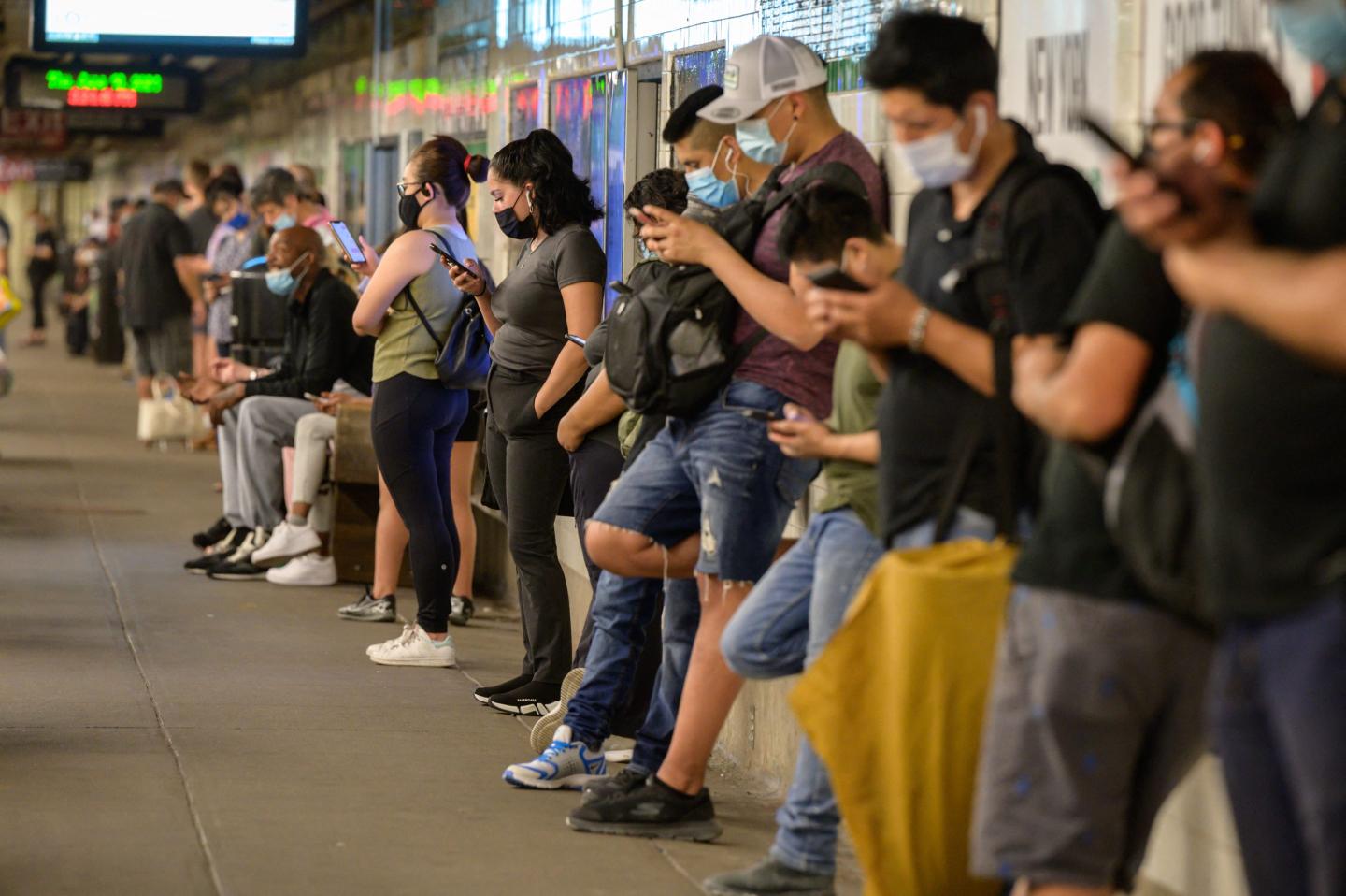 Commuters stand on the subway platform looking at their mobile phones.