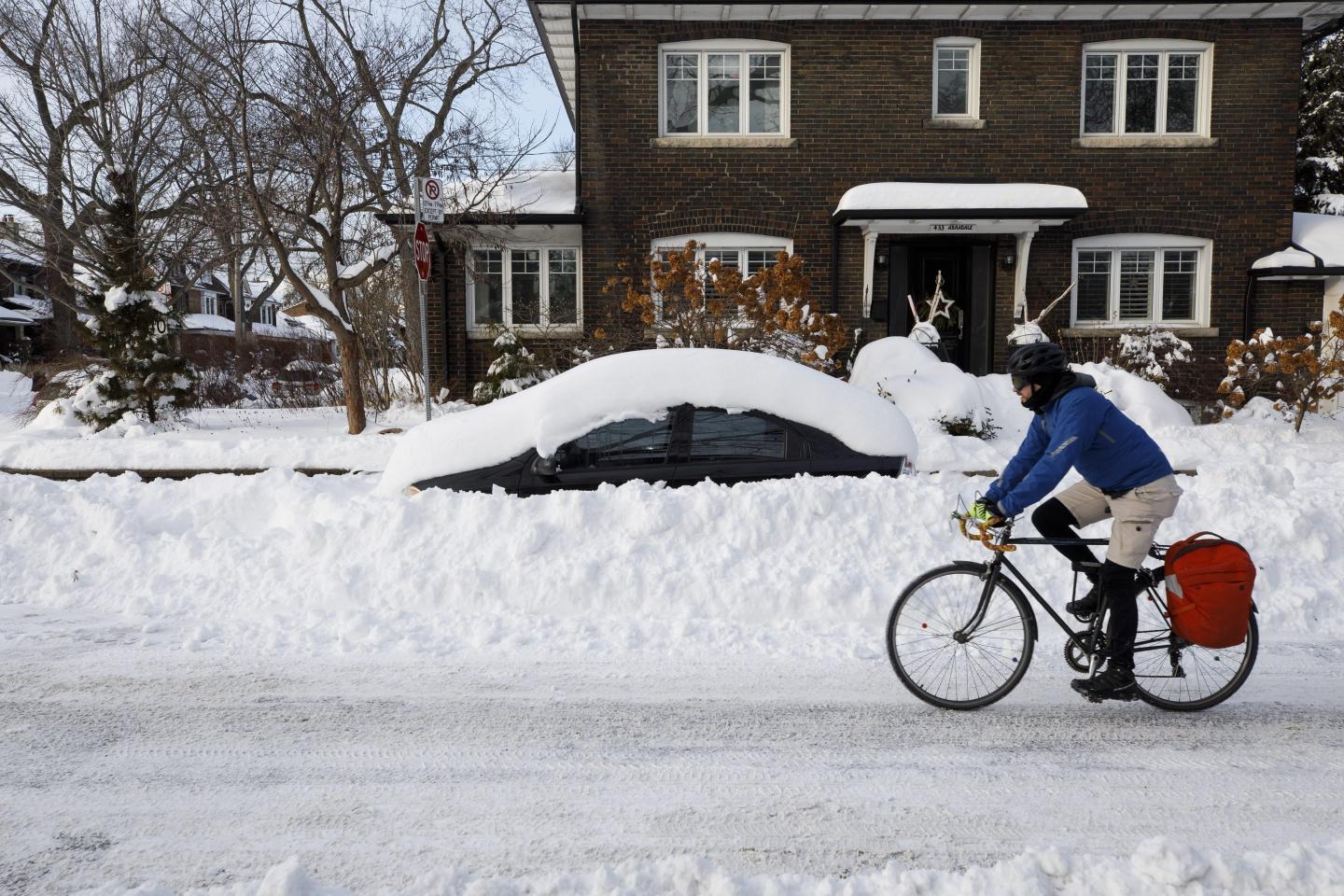 A cyclist bikes past a vehicle and house during a snowstorm in Toronto, Ontario, on January 18, 2022.