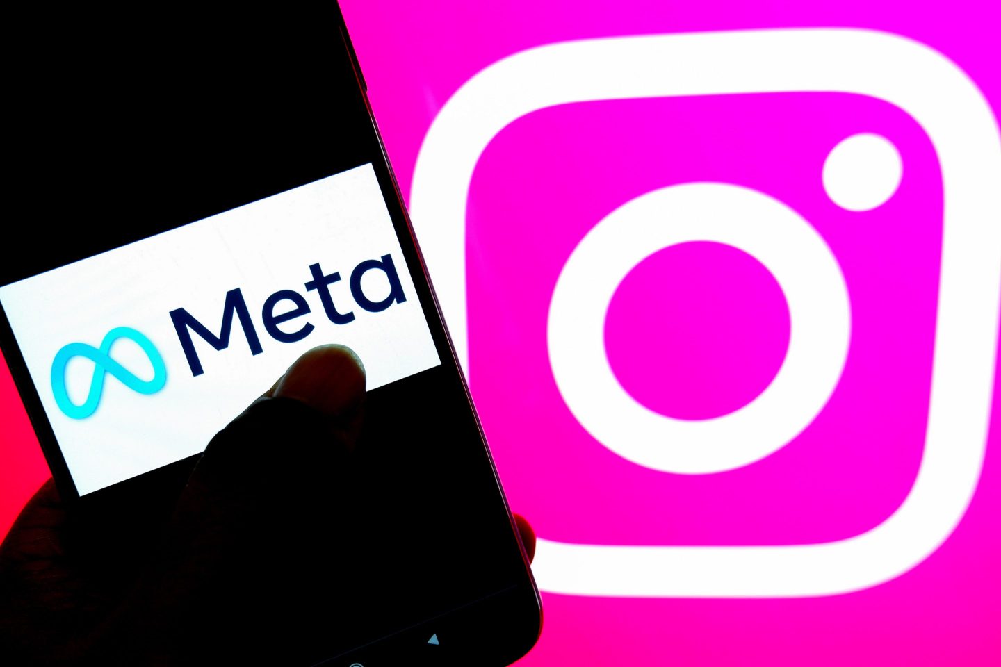 A Meta logo is seen on a smartphone with an Instagram logo in the background.