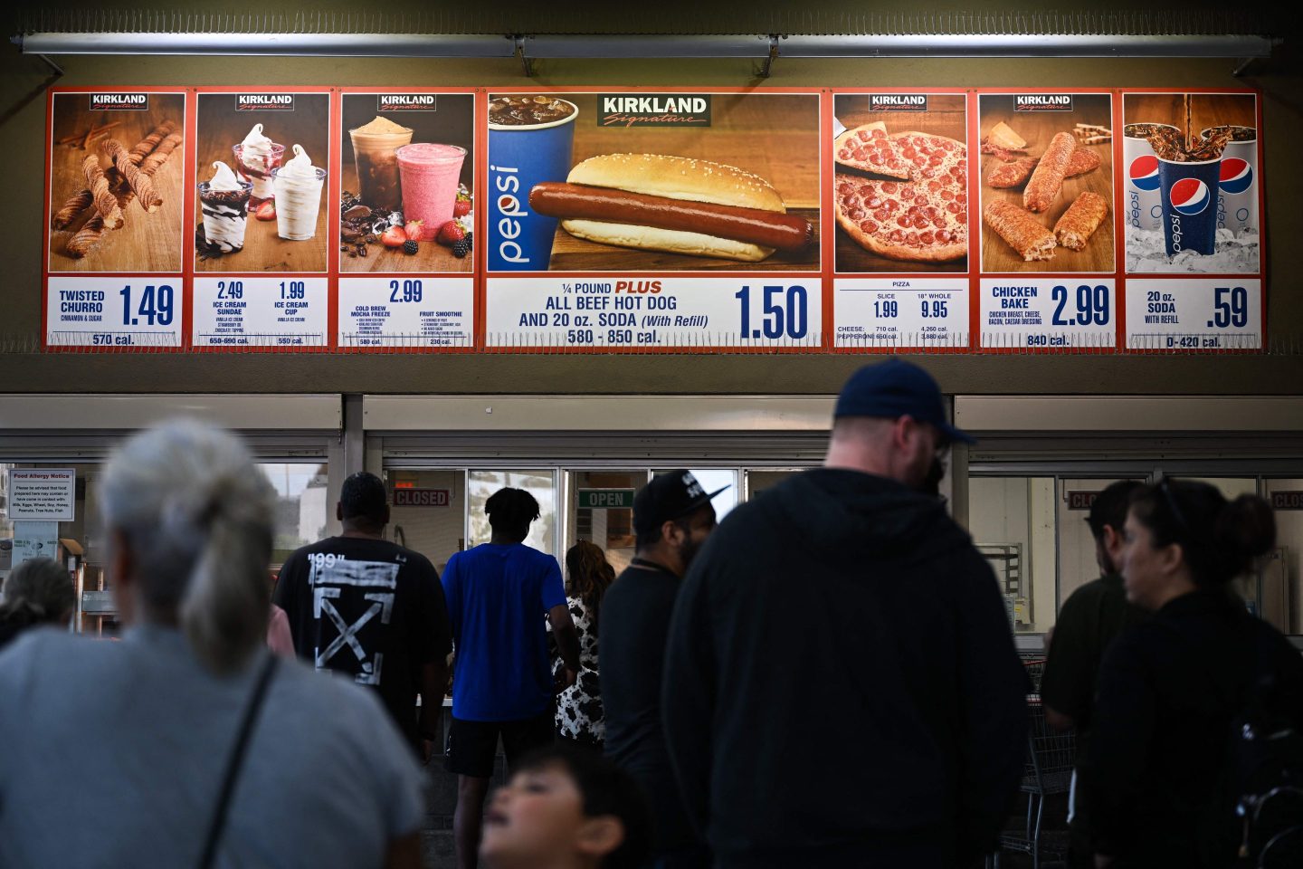 Customers wait in line to order below signage for the Costco Kirkland Signature $1.50 hot dog and soda combo