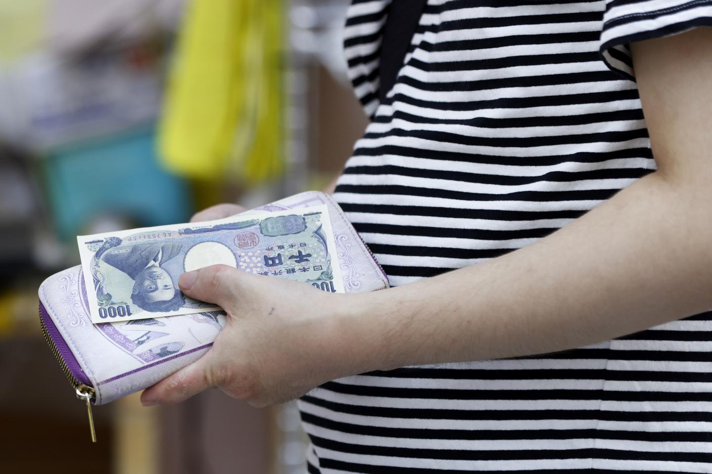 The image shows a shopper preparing to make a purchase with a 1,000 yen banknote in a Tokyo supermarket.