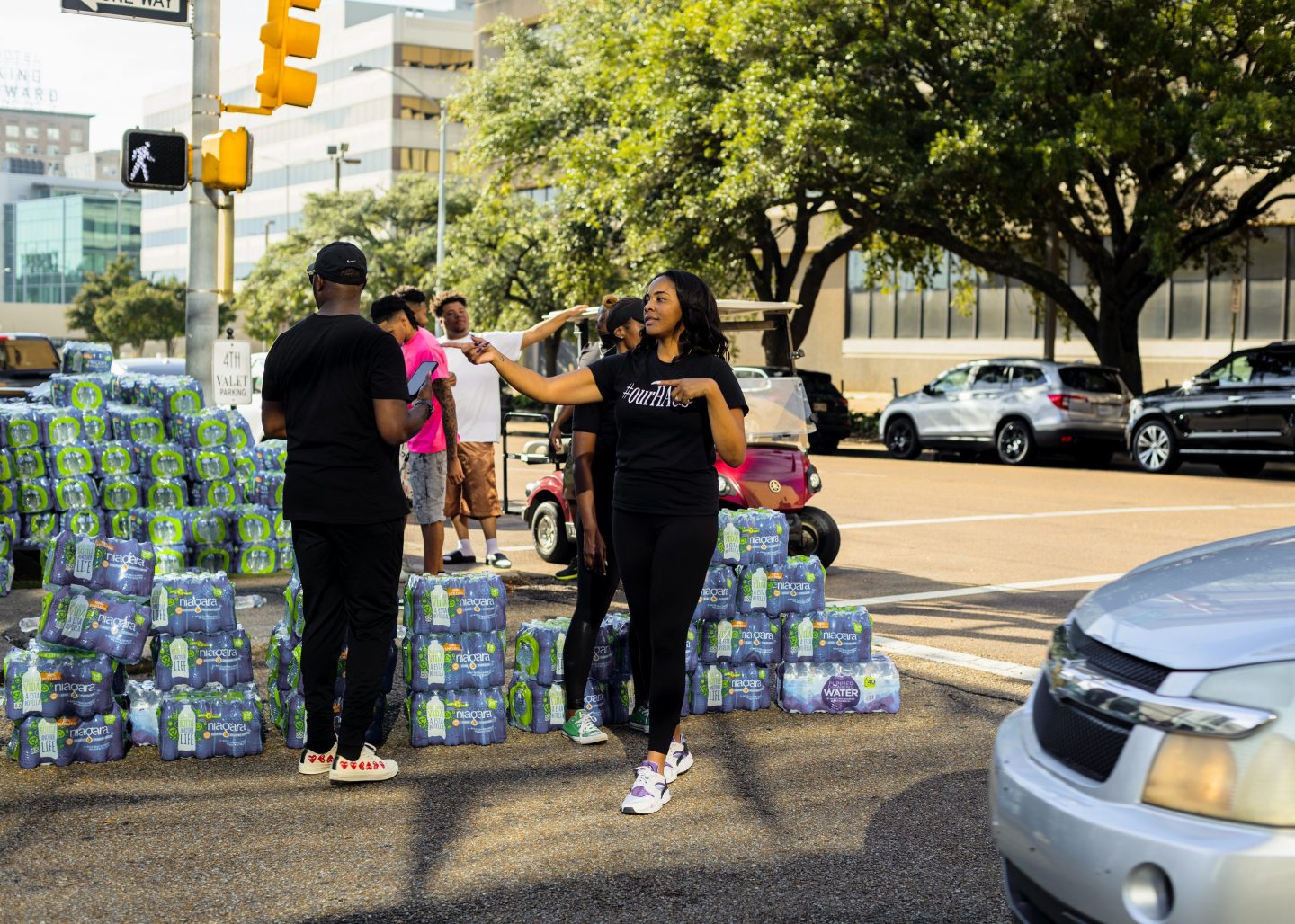 Stacks of water bottles line the street as cars pull up to pick from volunteers