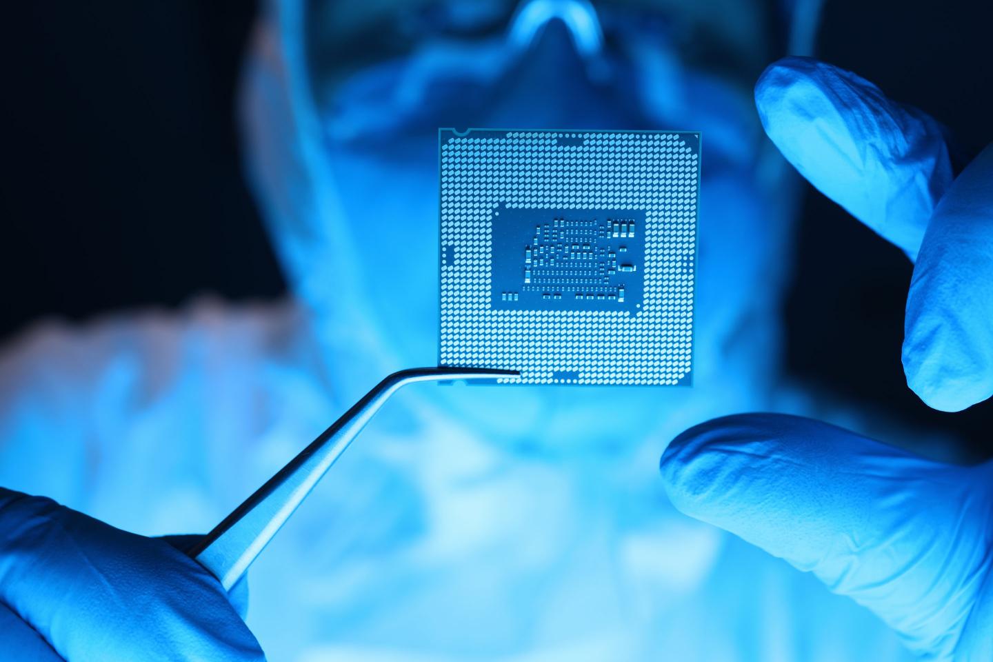 Man in a protective uniform holds a semiconductor microprocessing chip with a pair of forceps