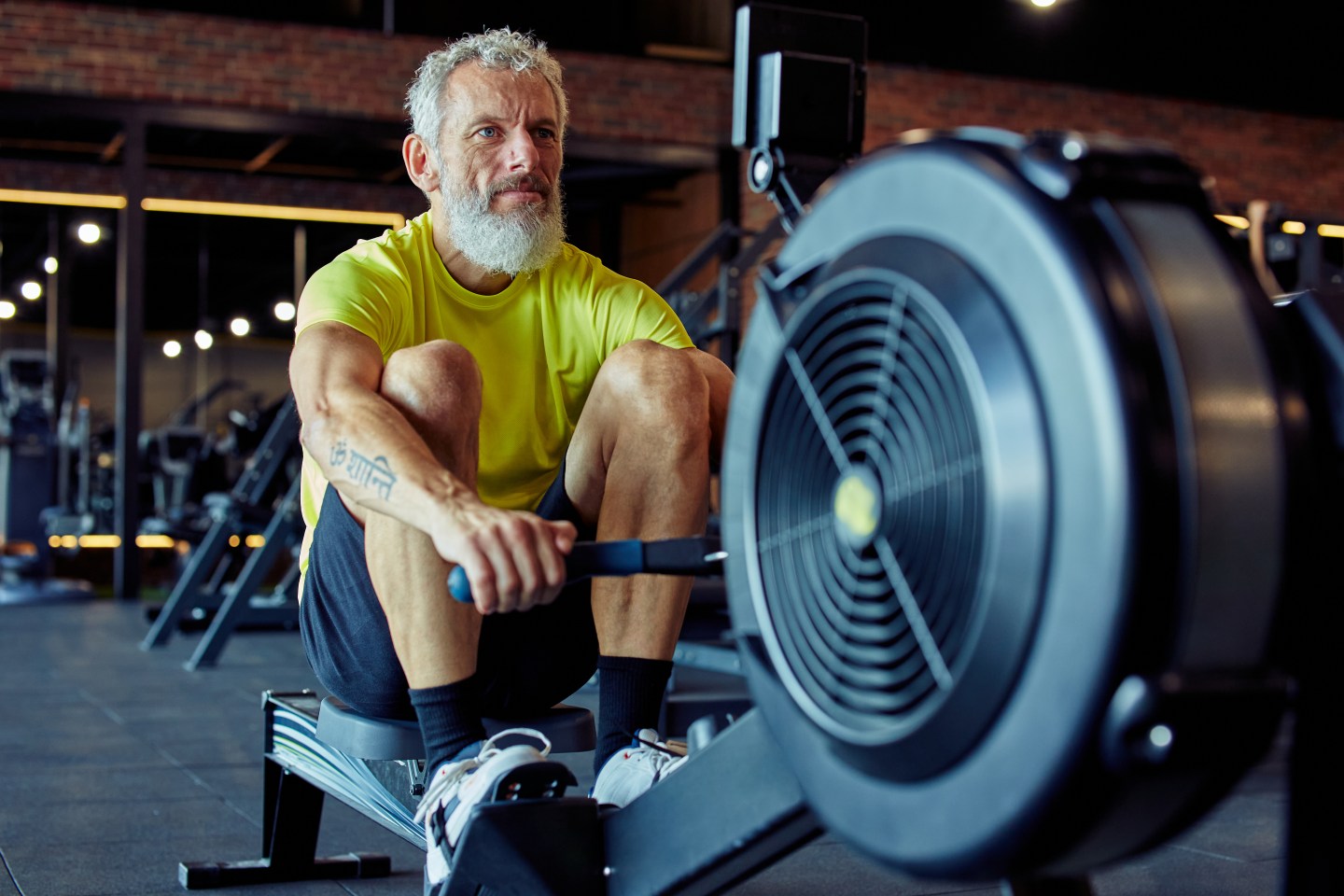 Strong mature athletic man in sportswear exercising on rowing machine at gym.