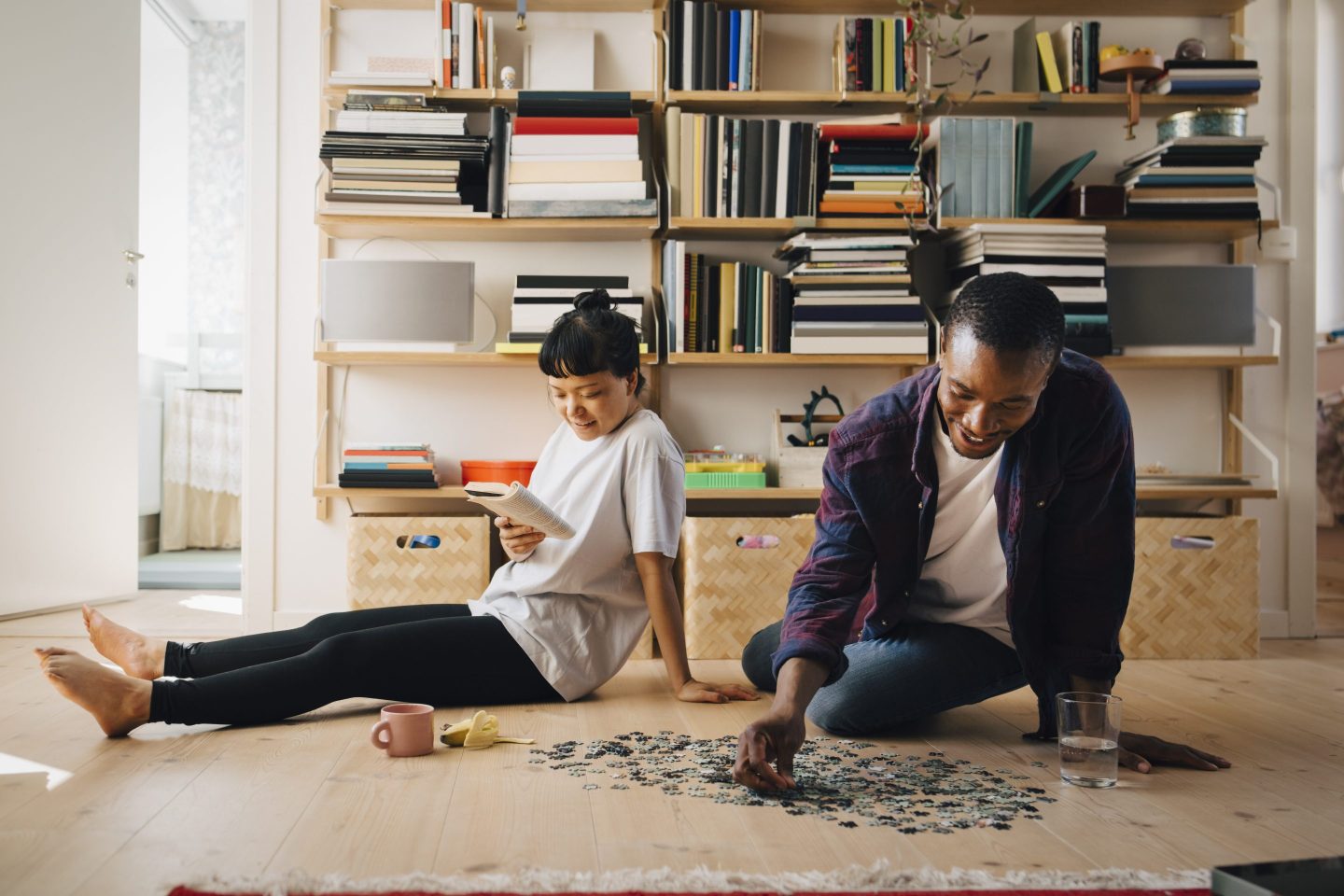 Man playing jigsaw puzzle while girlfriend reading book in living room