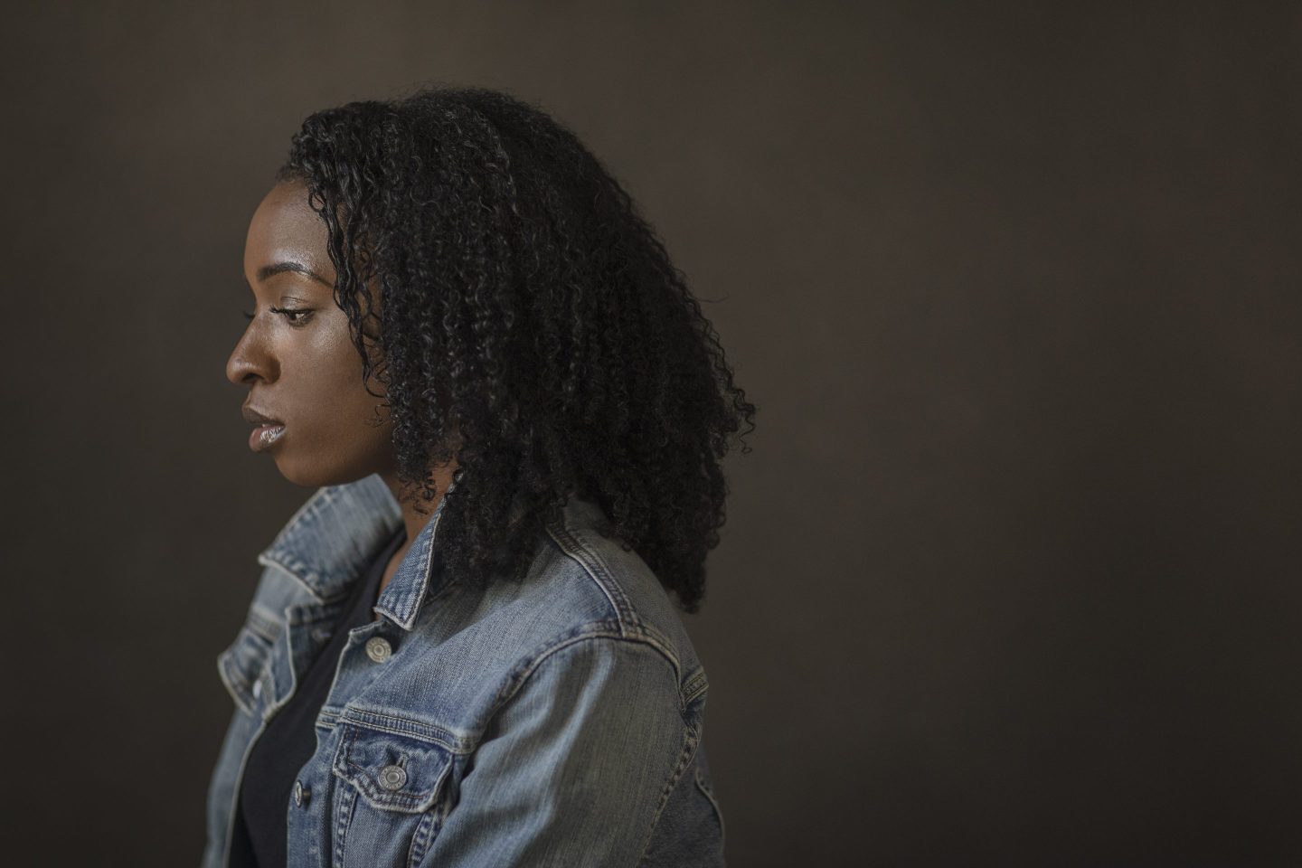 Sideview of sad young woman wearing denim jacket in studio