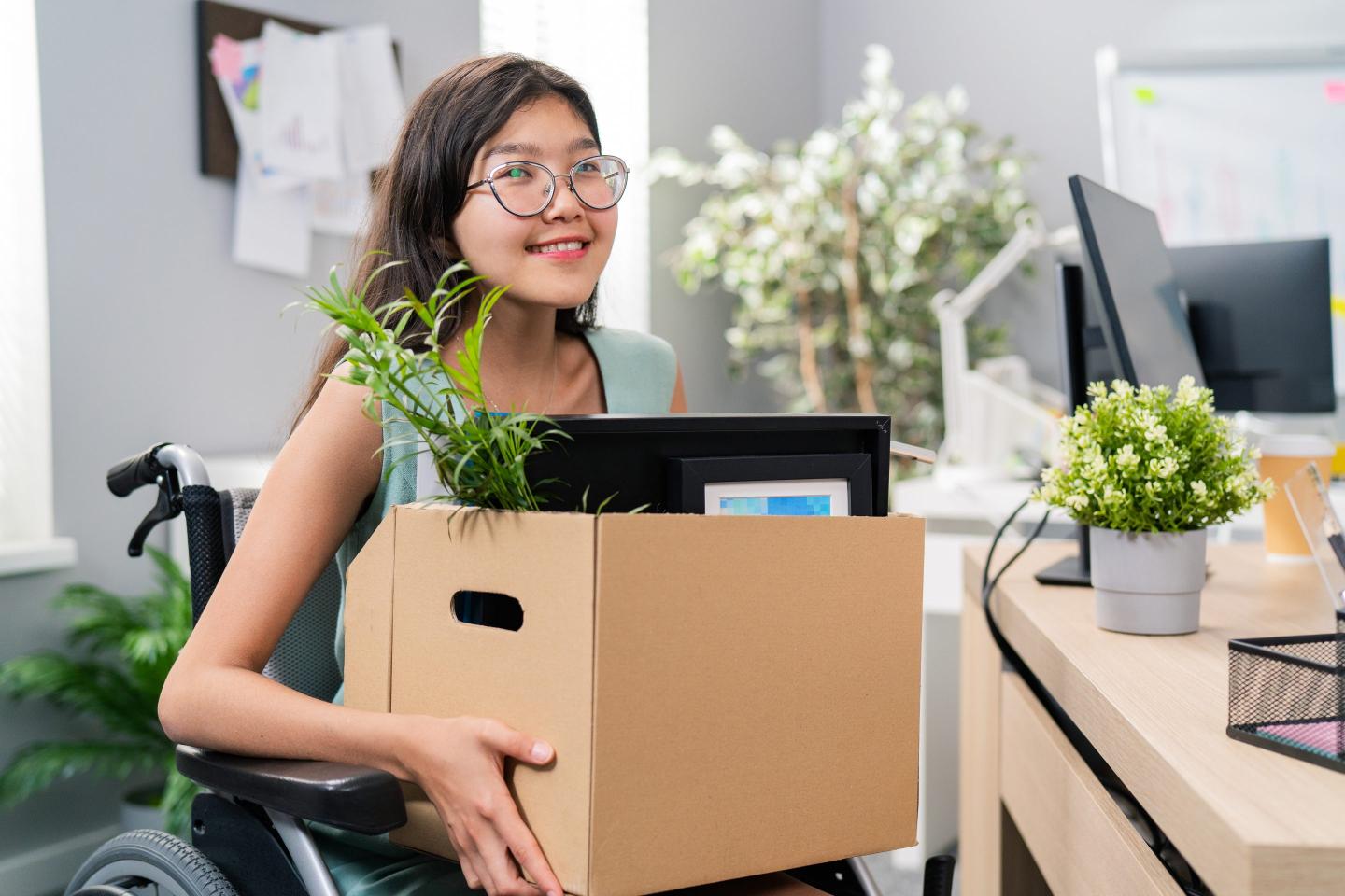 Woman in a wheelchair holding a box of her possessions leaving work