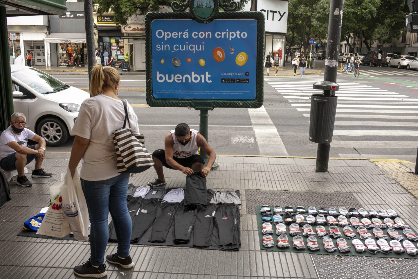 A street vendor offers clothes in front of virtual currency advisement in Buenos Aires, Argentina