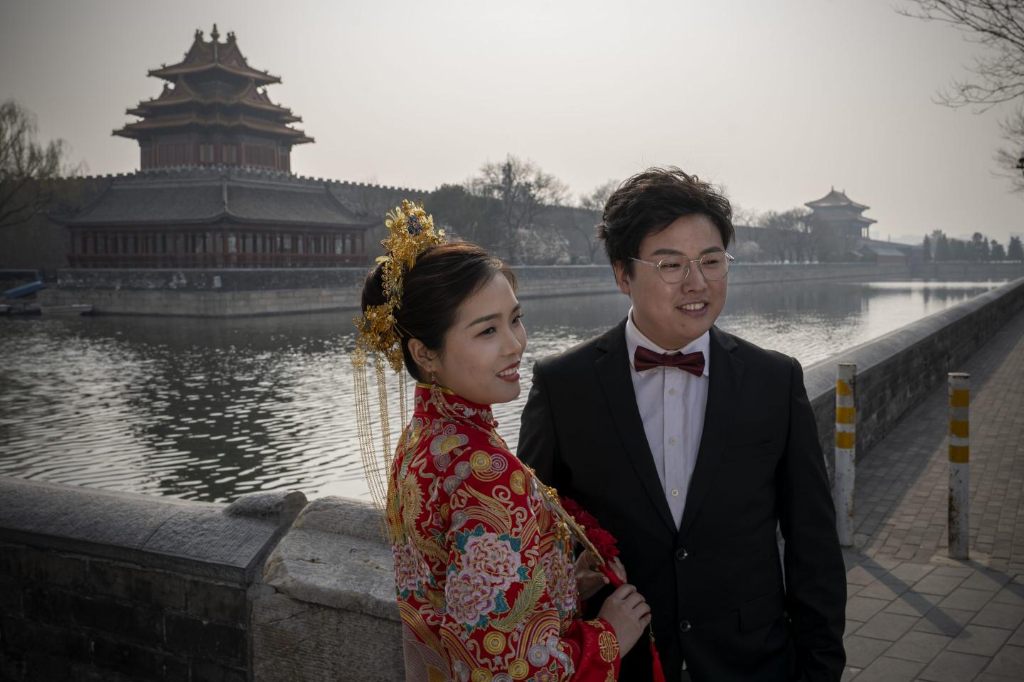 A bride and groom dressed in traditional wedding costumes pose in front of the Forbidden City in Beijing, China, on March 23, 2022.