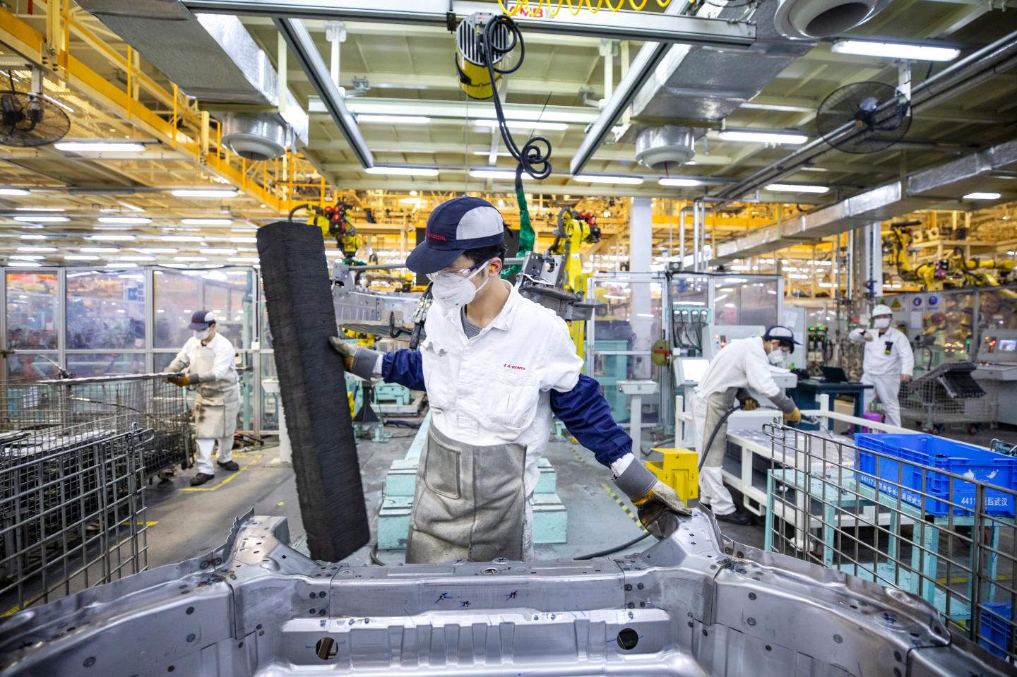 Shot of a worker assembling a car on a Honda assembly line with more workers in the background