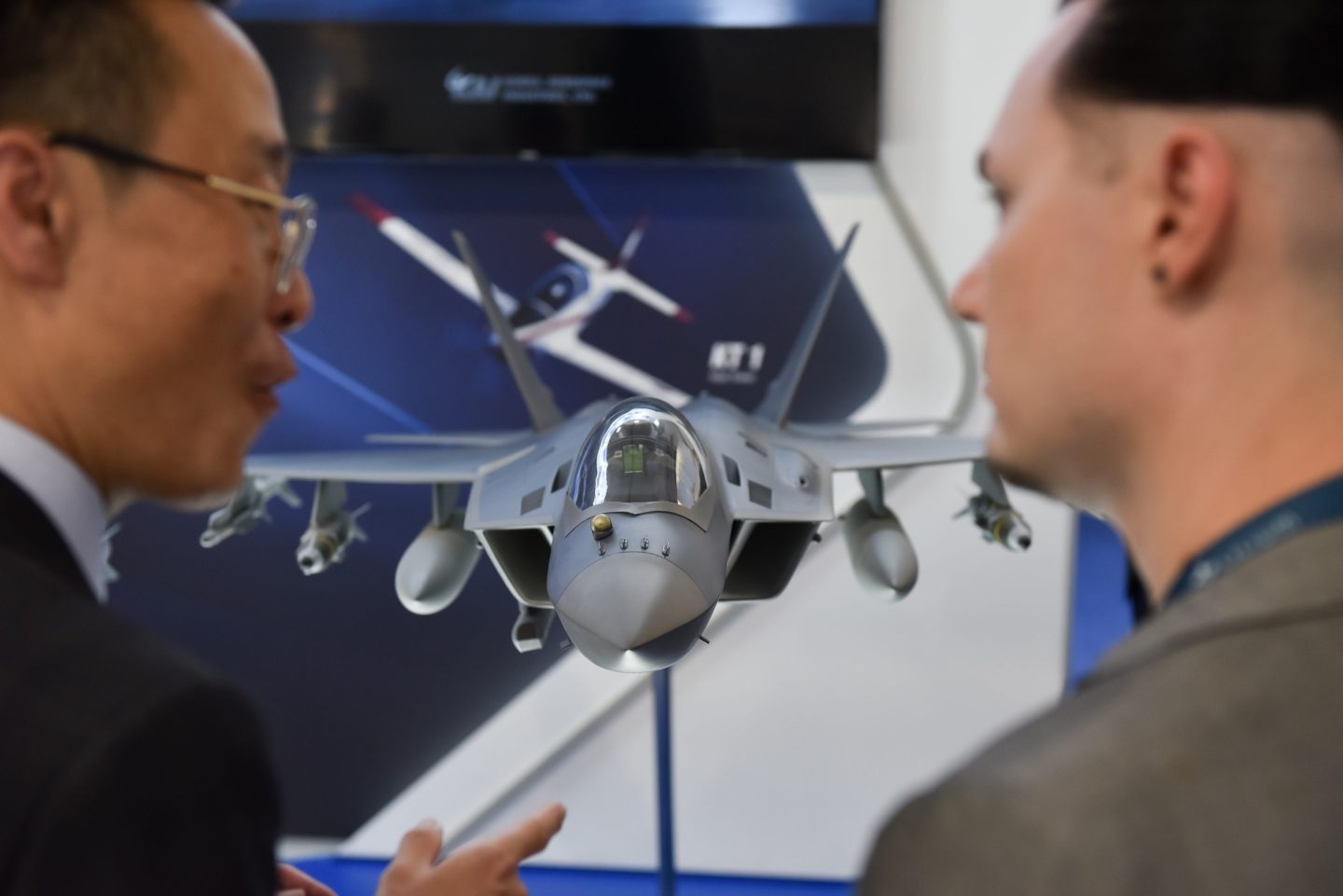 Two men look at a model of the Korean KF21 fighter jet