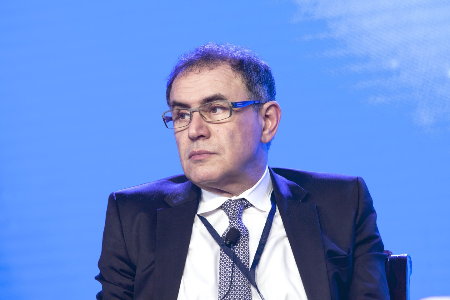 Shot of economist Nouriel Roubini sitting at a conference panel