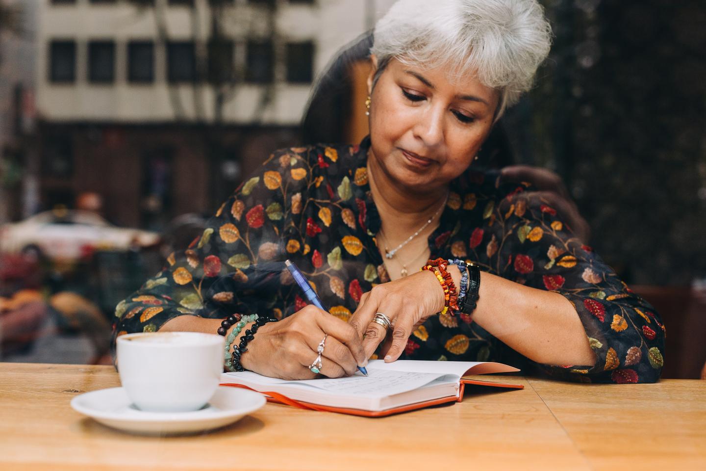 Middle Aged Woman Journaling In A Coffee Shop