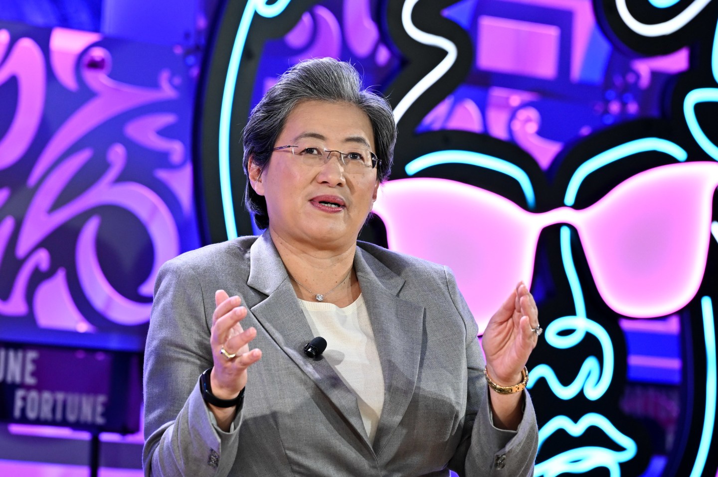 AMD CEO Lisa Su on stage in a gray suit, white undershirt, with hands up as she talks.