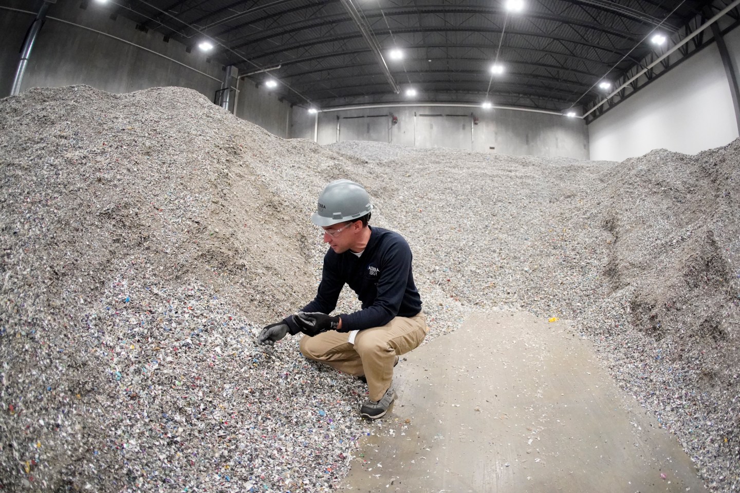 A man kneels down near a huge pile of shredded plastic.