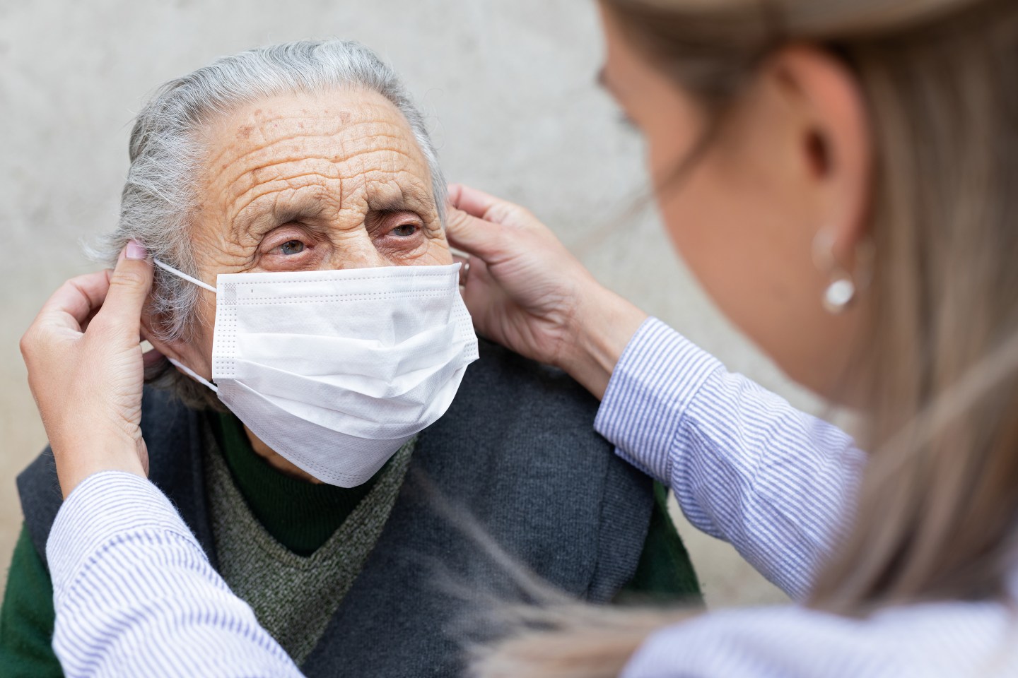 Nurse putting on surgical mask on elderly man.