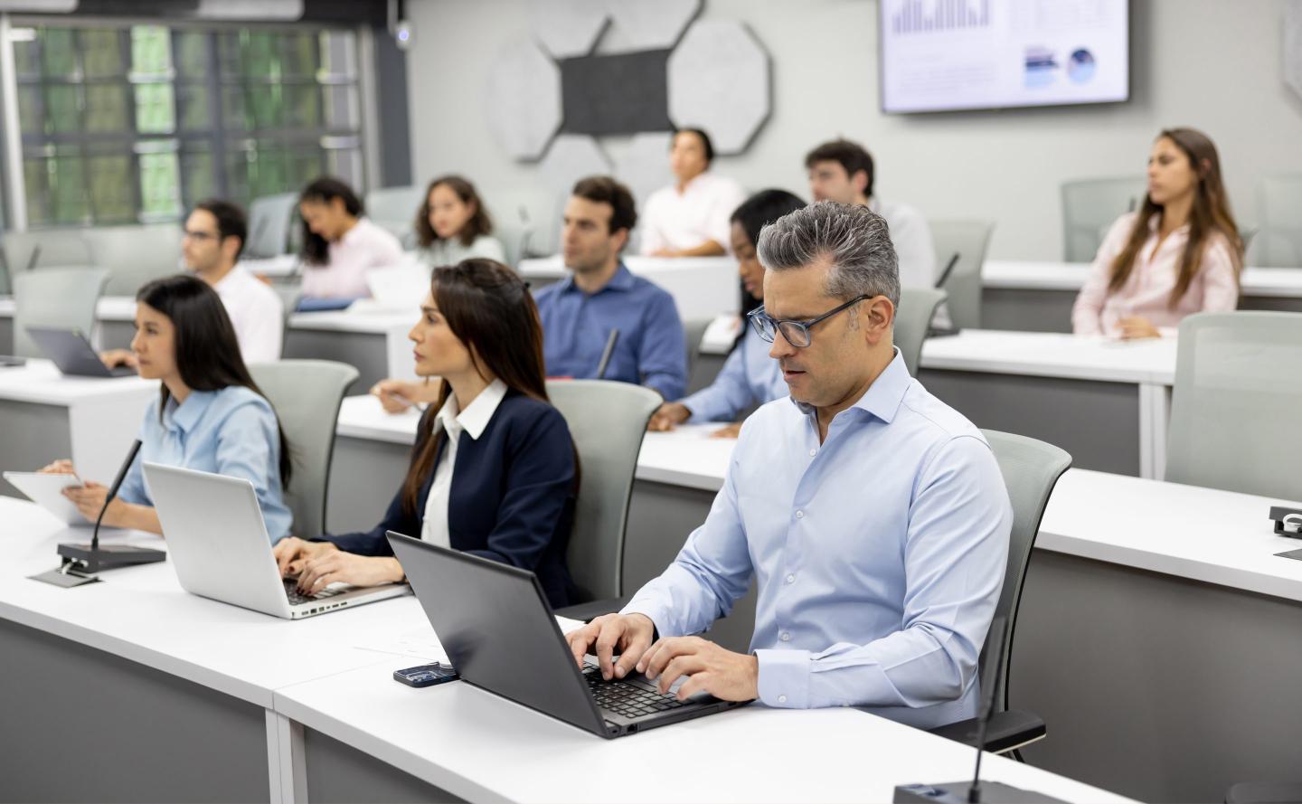 Group of MBA students sit using their laptops in a classroom.