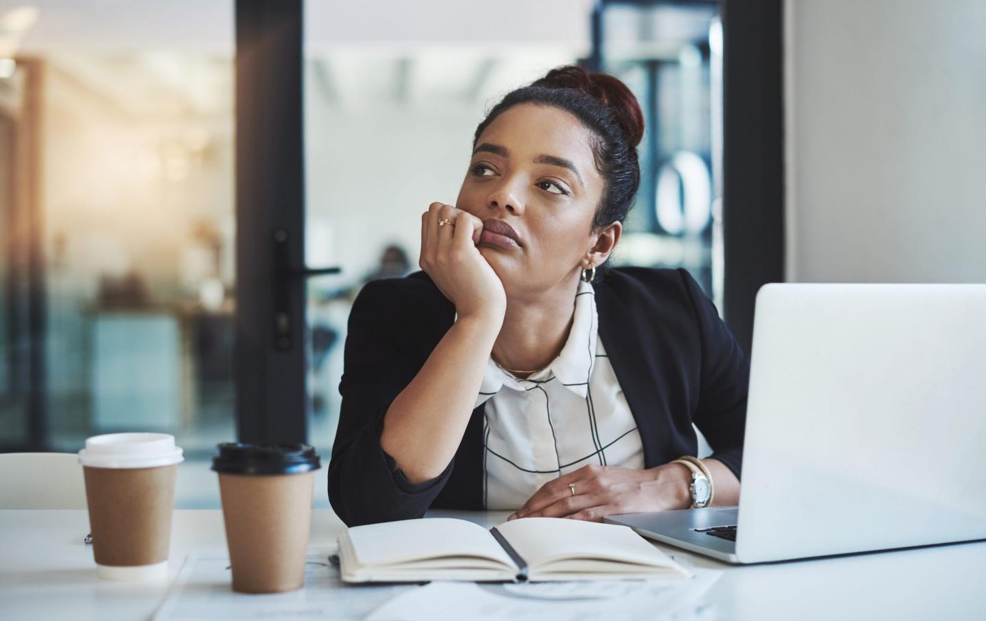 Woman looking bored with laptop and notebook nearby
