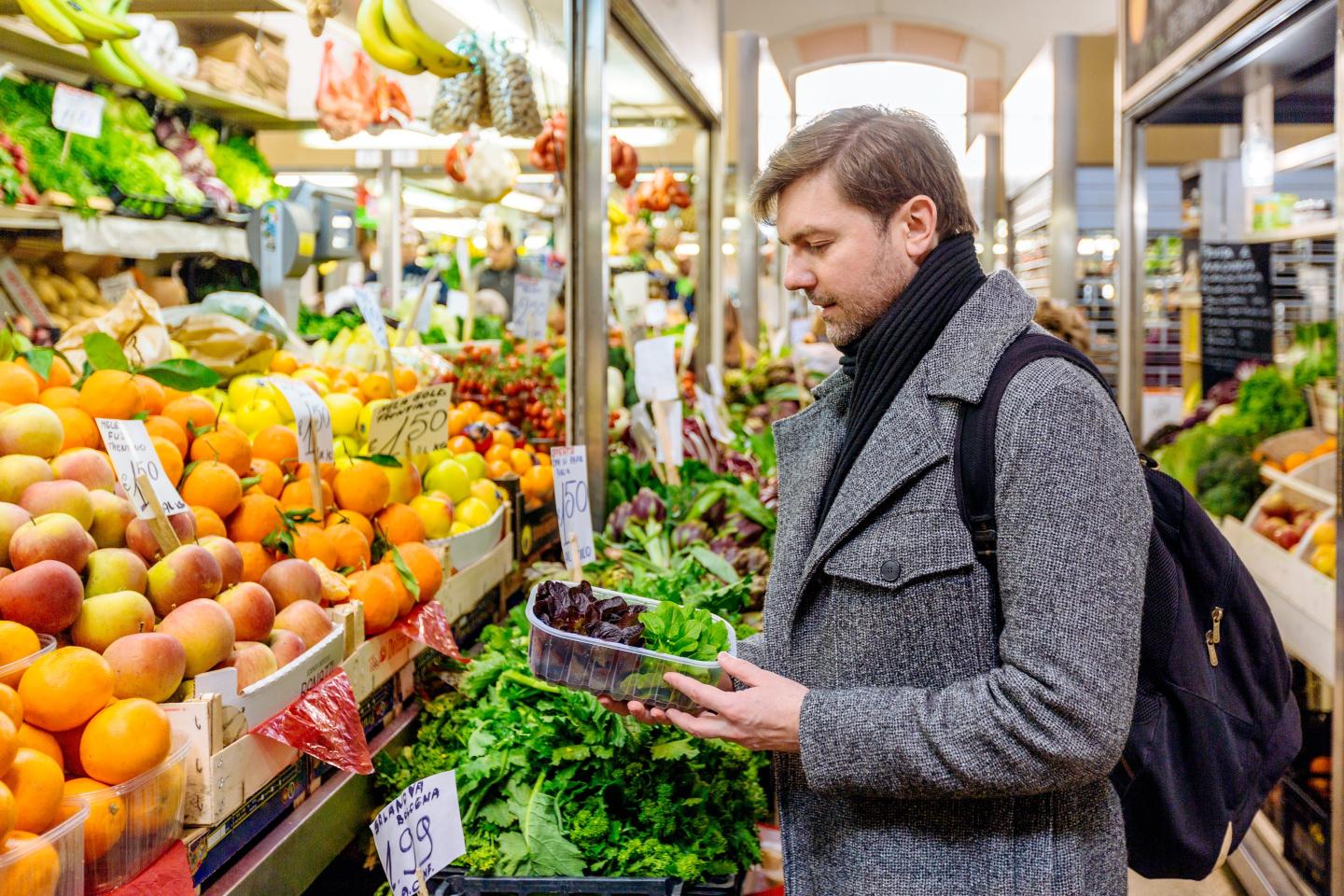 Shot of man buying groceries at a store, looking down at the price of a package of lettuce