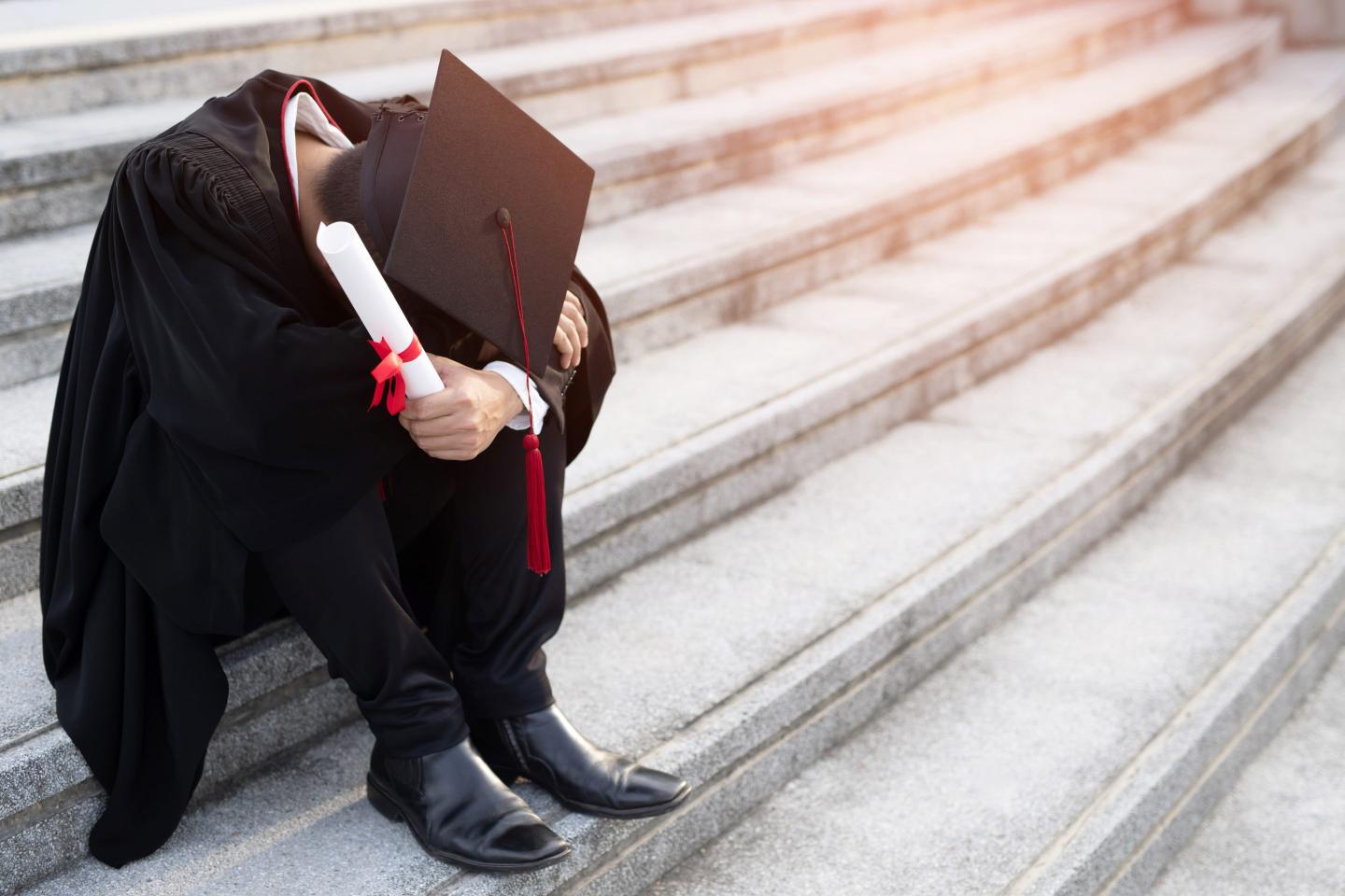 a graduate in cap and gown sitting on steps with head in lap