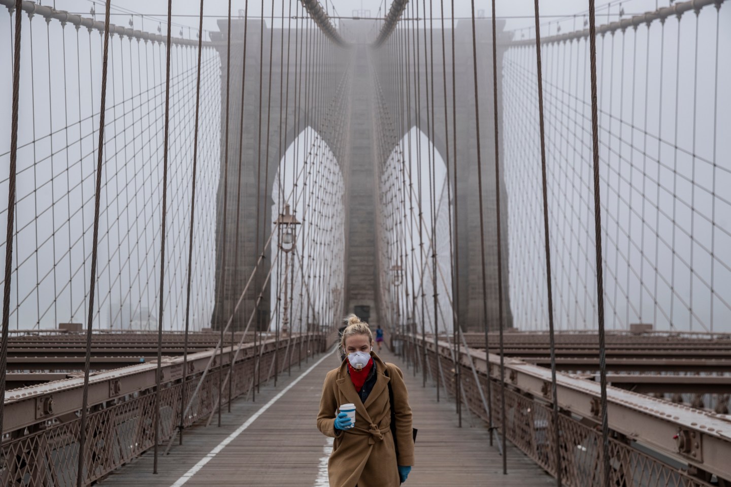 A woman walking across the Brooklyn Bridge.