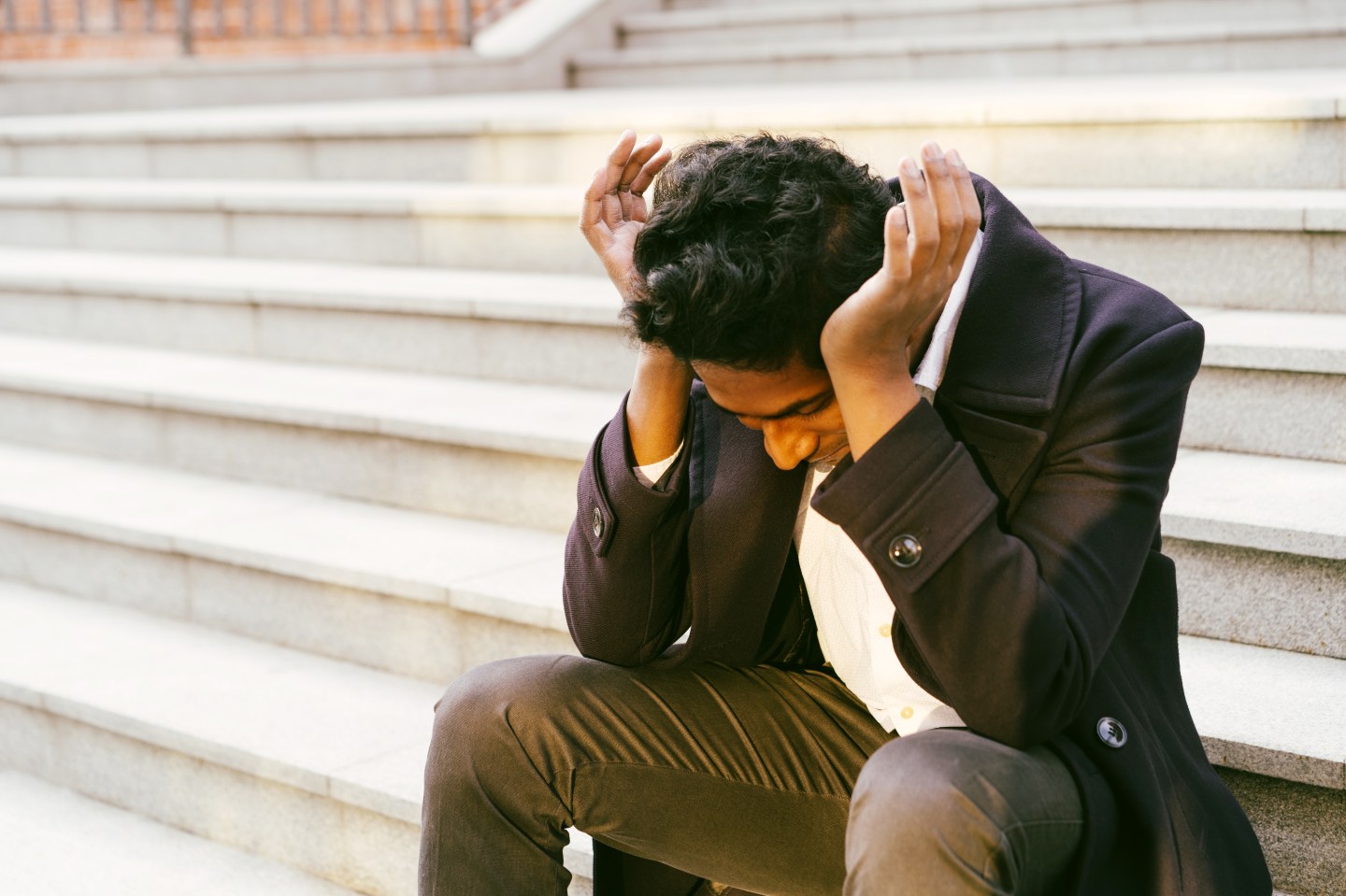 A stock photo of a banker sitting down holding his head in his hands.