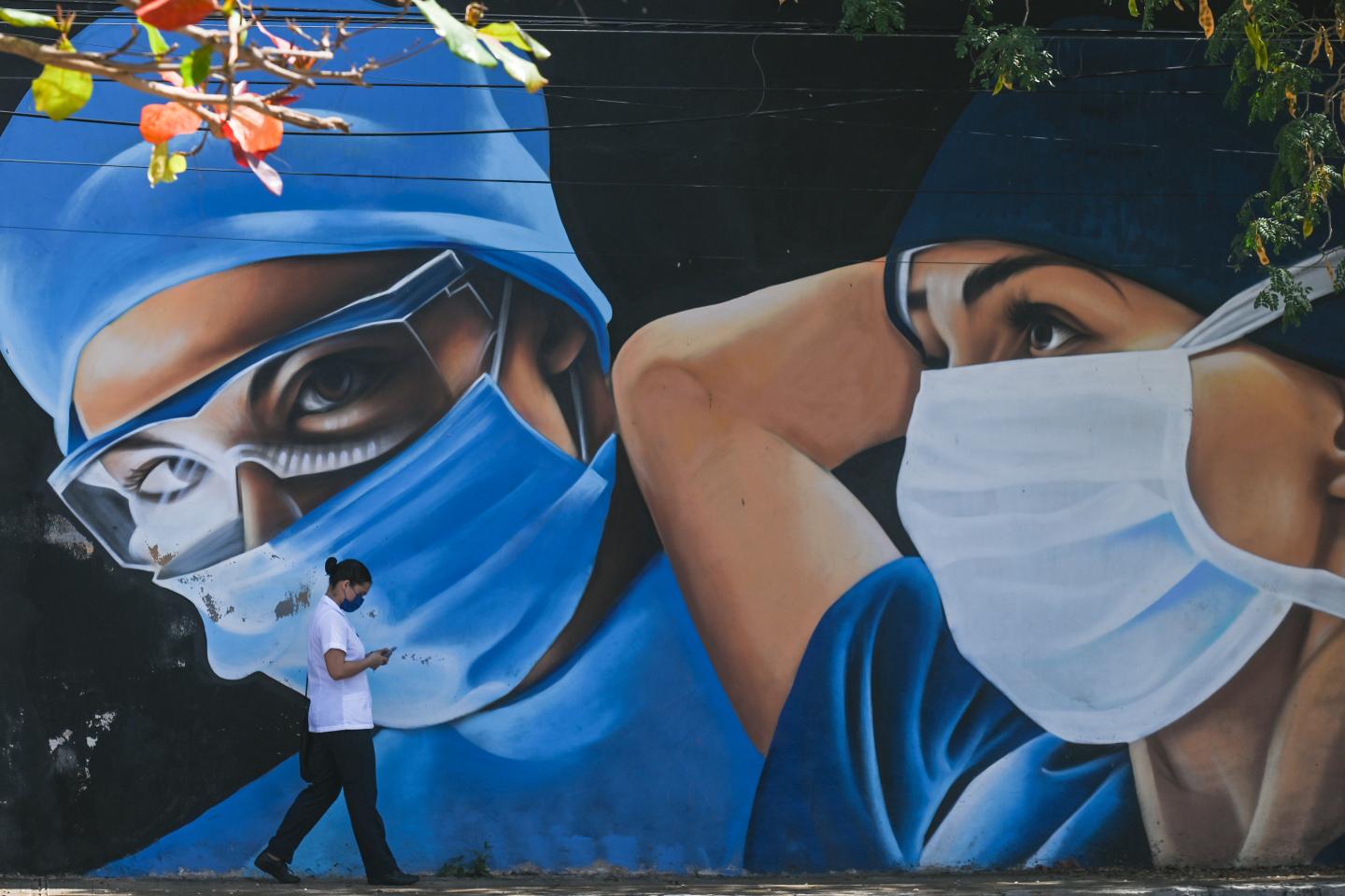 A woman wearing a face mask walks past a mural