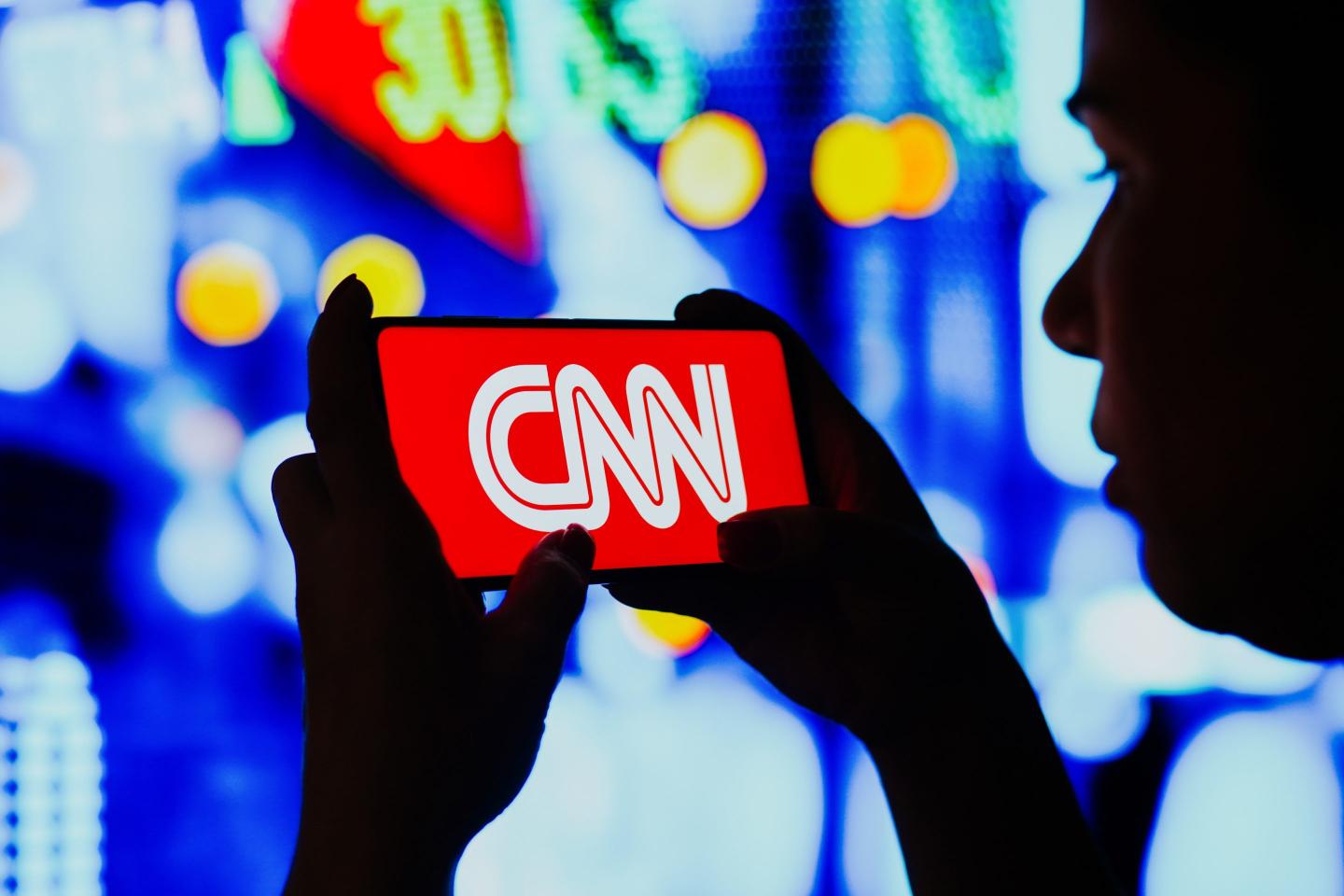 A woman holds a smartphone with the CNN logo displayed on the screen
