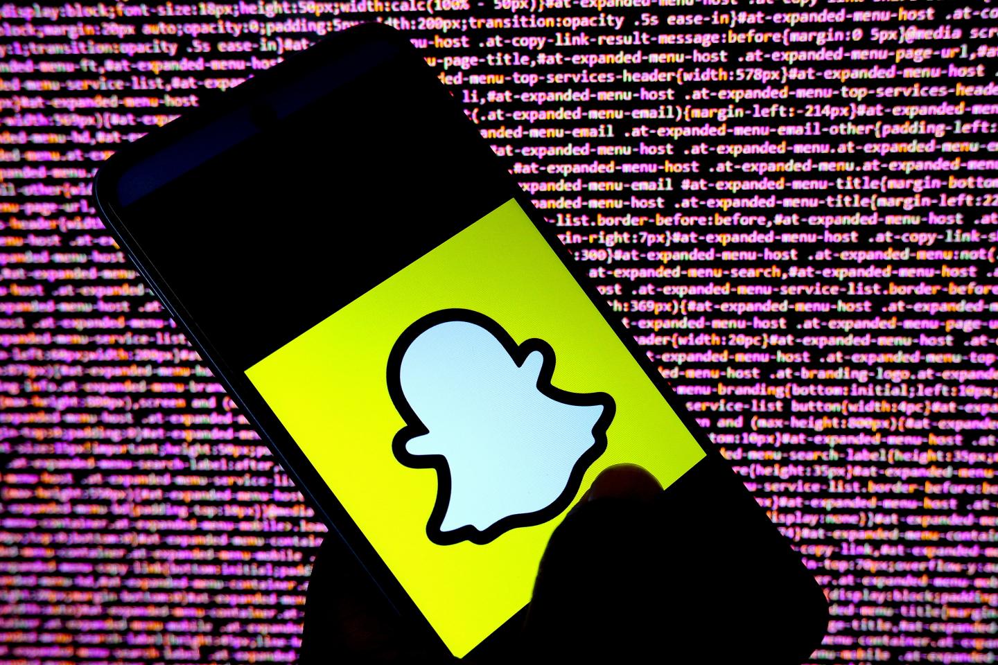 A person holding a smartphone that displays the Snapchat logo.