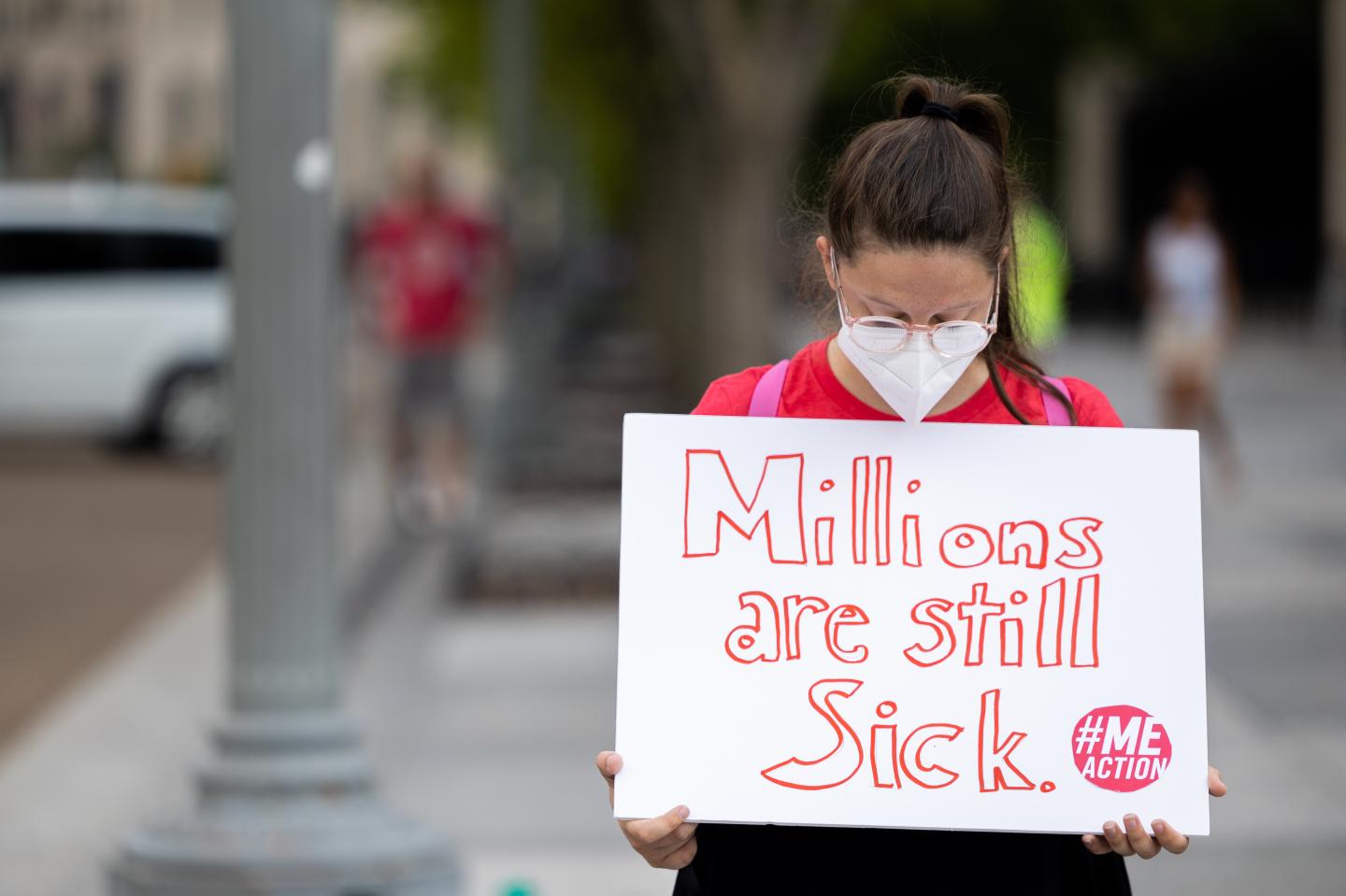 Protester holding a sign, "Millions are still sick."