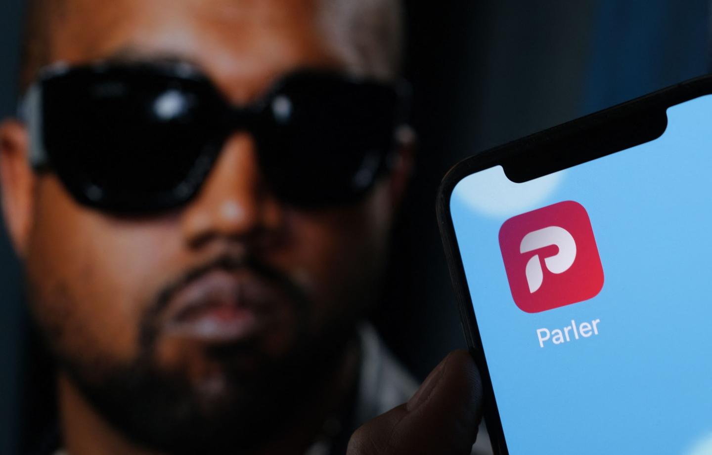 the Parler social network app logo on a cell phone screen with a picture of US rapper Kanye West in the background
