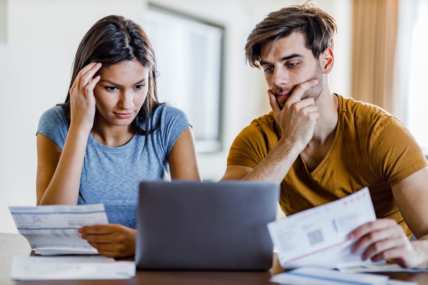 Young worried couple reading their financial bills over laptop at home.