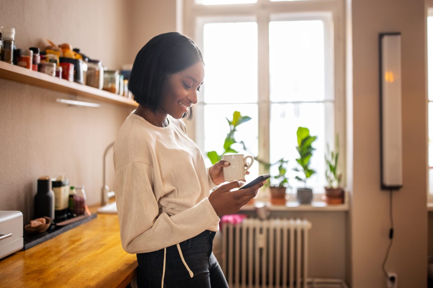 Woman having coffee and texting on her phone at home