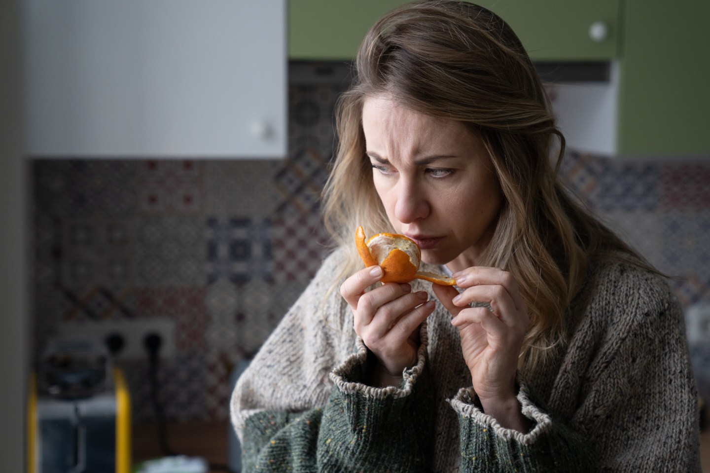 A woman attempts to smell an orange