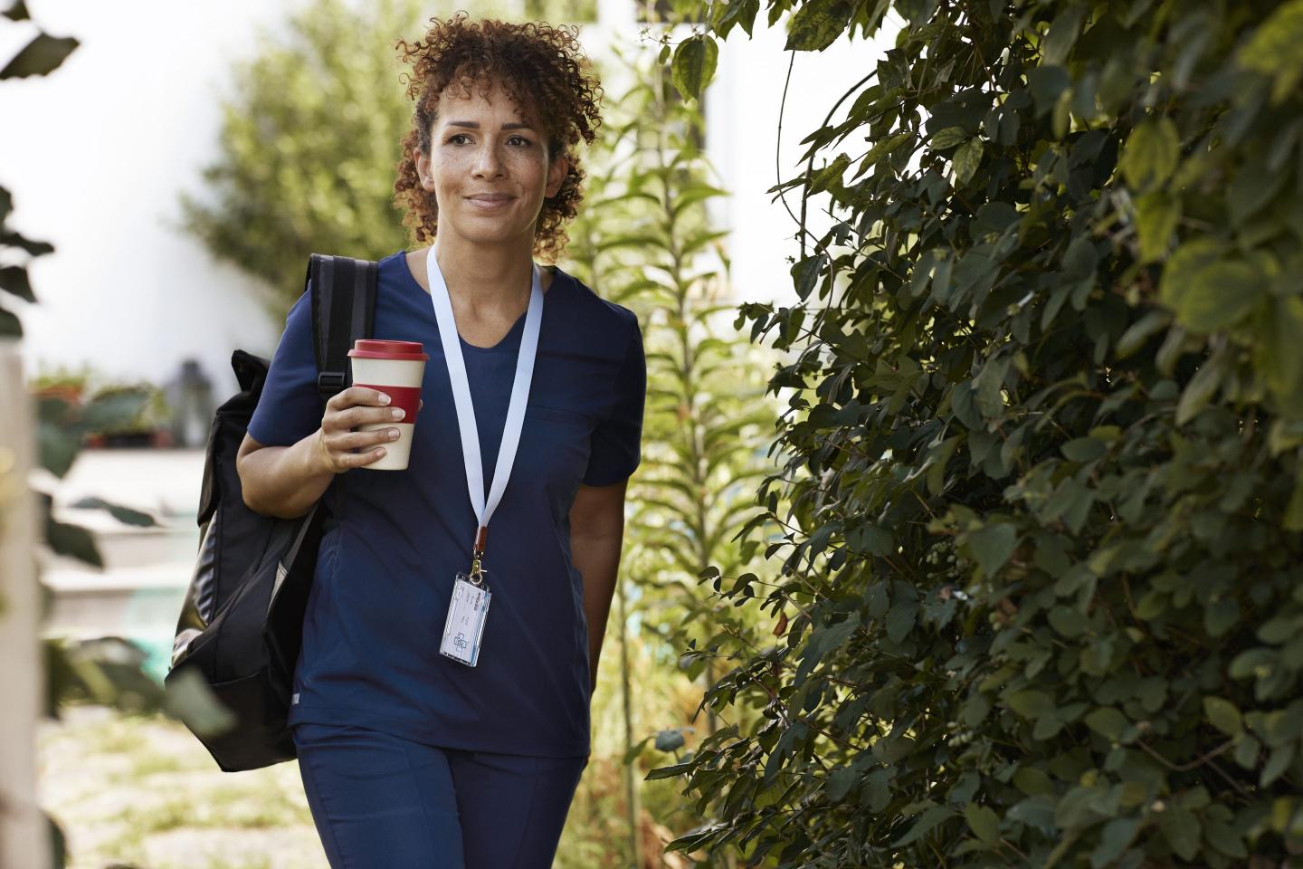 Caregiver with reusable cup walking by plants