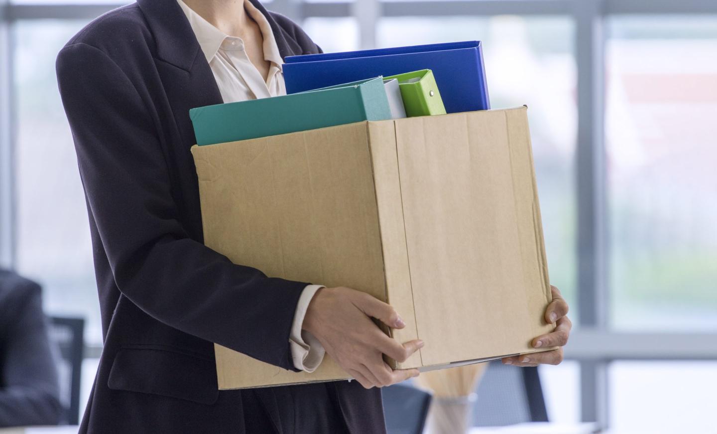 A laid-off employee carrying a box of belongings out of an office