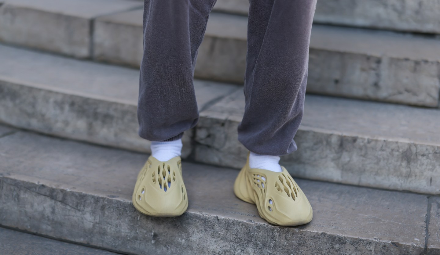 A guest seen wearing a dark grey jogger pants from Urban Outfitters, white socks and beige Adidas Yeezy Foam shoes, outside the Nahmias show, during Paris Fashion Week on June 23, 2022 in Paris.