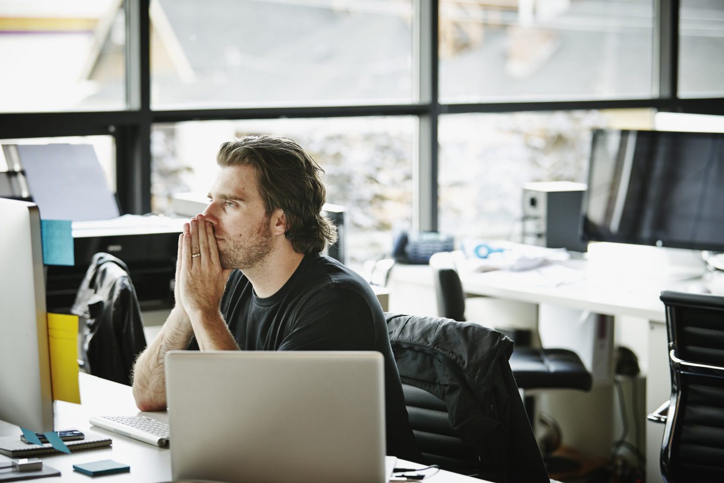 Businessman with hands on chin sitting at office workstation looking at computer monitor
