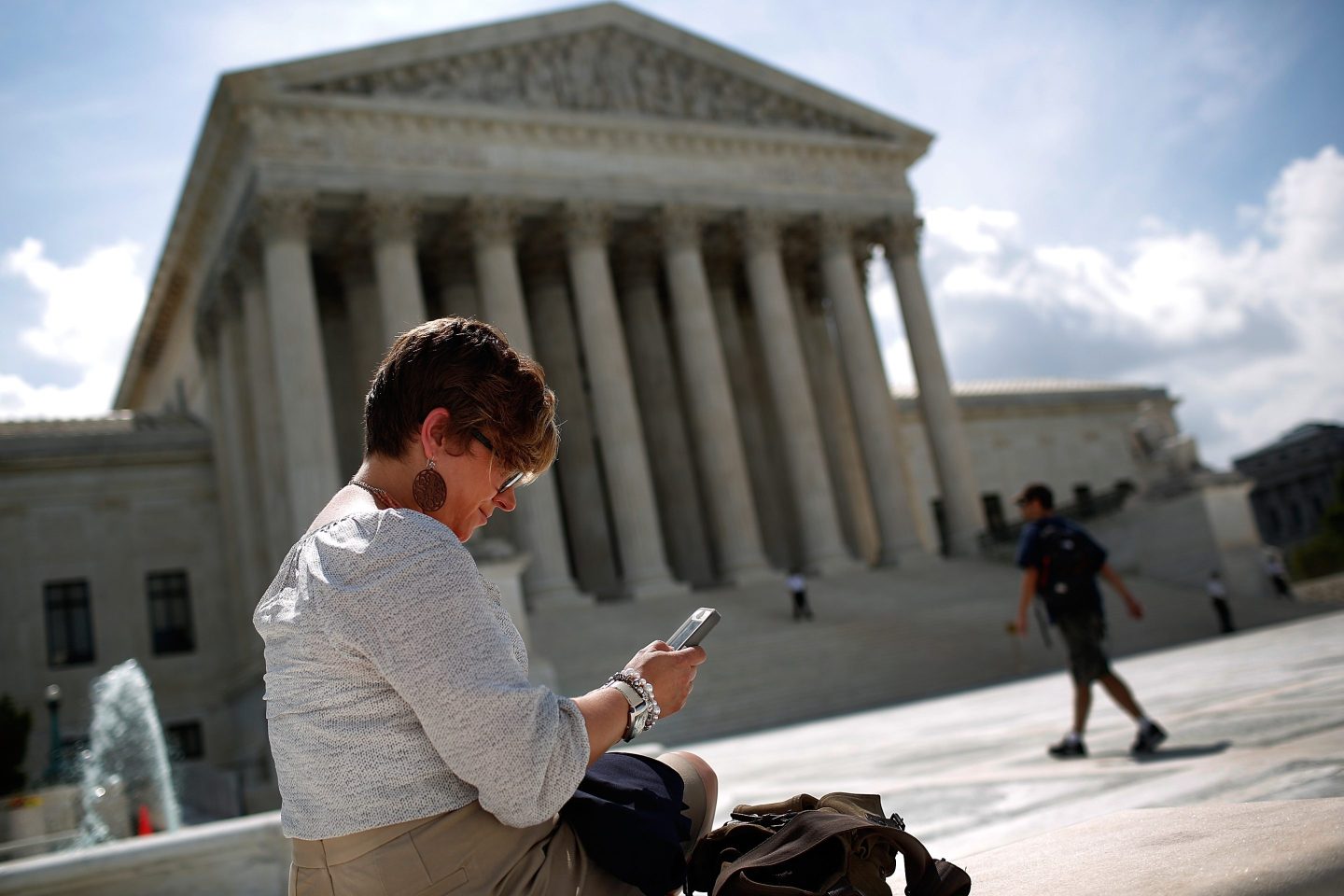 A woman with a phone sits in front of the US Supreme Court
