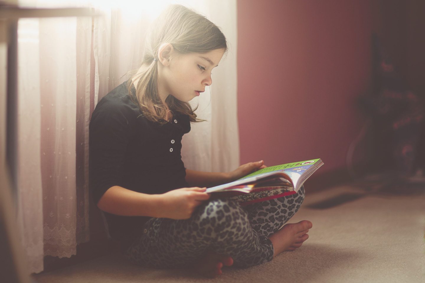 Girl reading, while seated on the floor, in her bedroom.