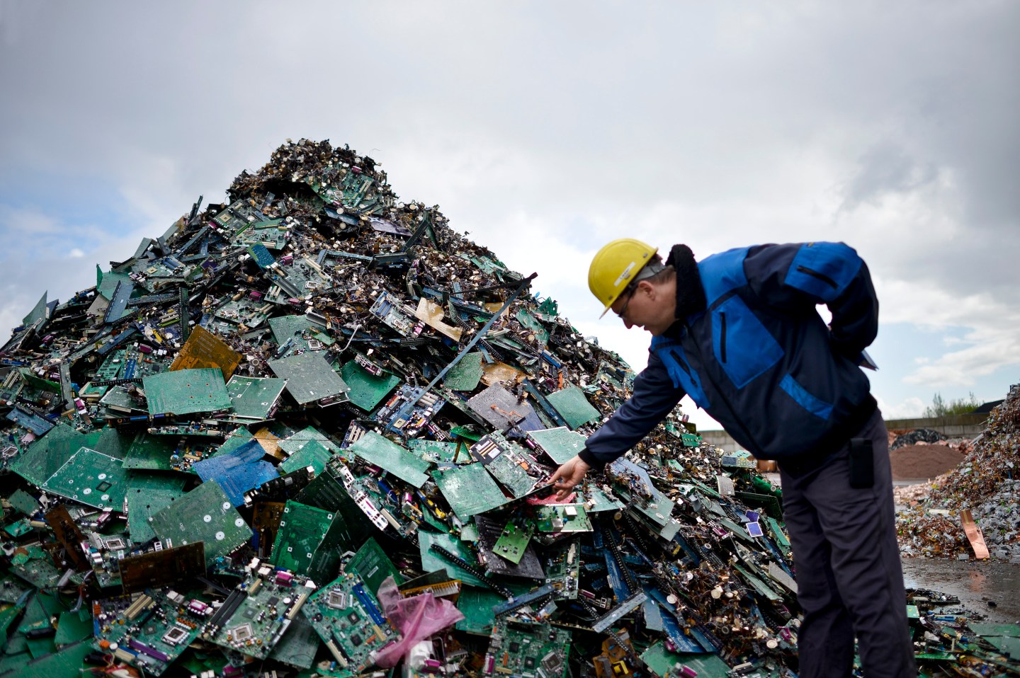 A man in hard hat stands near a pile of computer circuit cards junk