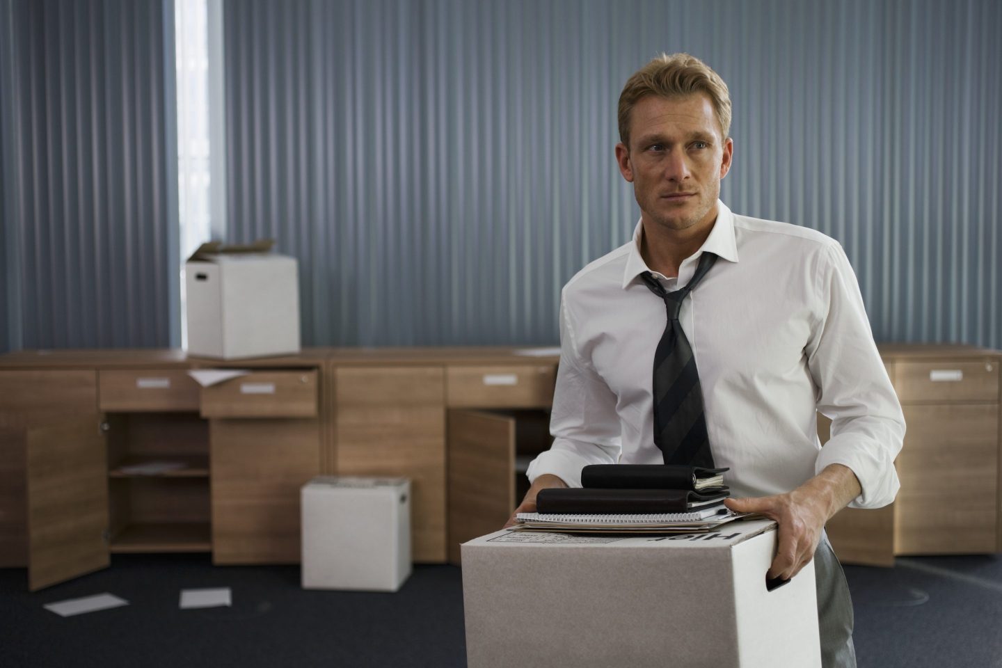 Shot of a laid off man in a shirt and tie leaving his office holding a box of items