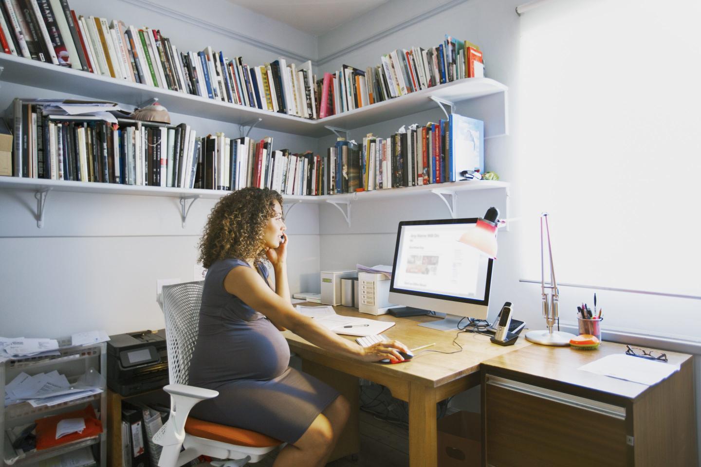 A pregnant woman works on a laptop