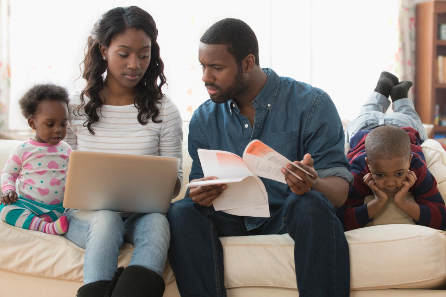Stressed parents looking over bills on a laptop while children play around them